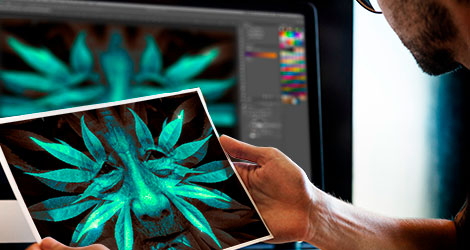 Ein Mann hält einen Fotoabzug in den Händen auf dem eine Bildcollage zu sehen ist. Im Hintergrund befindet sich ein Compputermonitor, welcher die gleiche Bildcollage in Adobe PhotoShop zeigt.